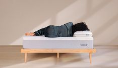 a person laying on top of a mattress with no sheets or pillows in front of a wall