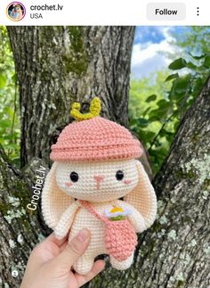 someone is holding up a small crocheted stuffed animal in front of a tree