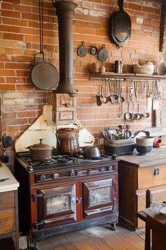 an old fashioned kitchen with pots and pans hanging on the brick wall above the stove