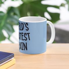 a blue coffee mug sitting on top of a wooden table next to a book and plant