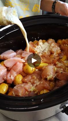 someone pouring milk into a slow cooker filled with meat and potatoes, ready to be cooked