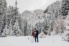 a bride and groom kissing in the snow surrounded by pine trees on their wedding day