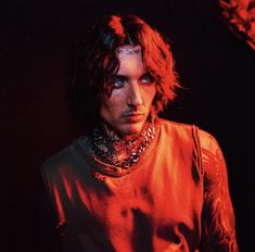 a man with long hair wearing a red shirt and chain necklaces on his neck