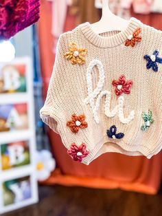 a white sweater with flowers on it hanging from a clothes line in a store window