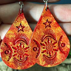 Crimson suns with spiral centers, stars, and moon shapes add celestial magic to these bright, handcrafted leather earrings, with carnelian accent beads. Generously sized but light as a feather.  Lightweight and comfortable, I cut these from vegetable tanned leather, and stamped designs into their surface. Then I dyed them red, and surface textured them with golden yellow and warm orange tones, to accent the tooled design. I sealed them for water resistance, suspended them under carnelian beads, and finally, fastened them to a pair of hypoallergenic french hooks: surgical steel.  One of my photos shows the earrings next to a standard US quarter, for size reference.    P.S. My model is a mannequin, so these earrings have never been in human ears. You will receive the exact earrings that I ph Orange Teardrop Jewelry For Festivals, Handmade Red Star Jewelry, Bohemian Star-shaped Jewelry For Festivals, Bohemian Star Jewelry For Festivals, Bohemian Star-shaped Festival Jewelry, Spiritual Sun Design Jewelry For Festival, Spiritual Sun And Moon Design Earrings For Festival, Adjustable Spiritual Earrings With Sun And Moon Design, Adjustable Sun And Moon Spiritual Earrings