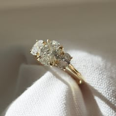 three stone diamond ring sitting on top of a white cloth in the sunlit room