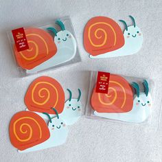 three orange and white snail shaped coasters on a white surface with tags attached to them