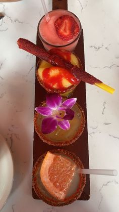 three desserts are arranged on a tray with strawberries, orange slices and an orchid