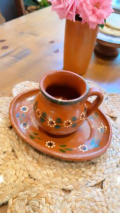 a brown vase with pink flowers sitting on top of a table next to a cup and saucer