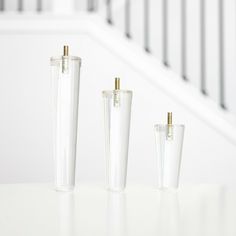 three clear glass vases sitting on top of a white table next to a stair case