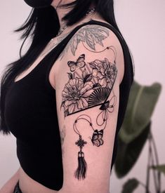 a woman with a tattoo on her arm holding a fan and flowers in the background