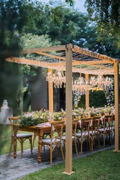 an outdoor dining set up with chandelier hanging from the ceiling and flowers on the table