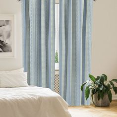 a white bed sitting next to a window covered in blue and white striped drapes