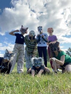 several people wearing masks in the grass with cats on their heads and one person taking a selfie