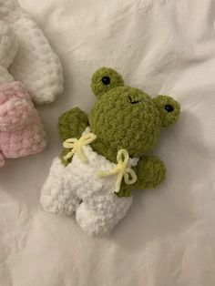 three crocheted stuffed animals laying on top of a white bed sheet, one is green and the other is pink