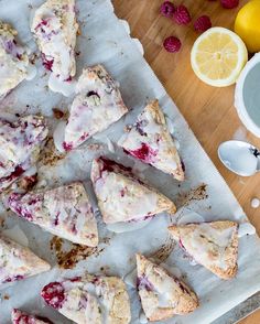 lemon and raspberry scones on parchment paper next to sliced lemons, berries, and sugar