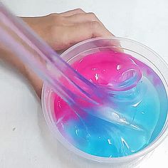 a hand holding a pink and blue liquid in a plastic cup