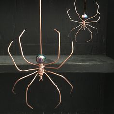 two metal spider sculptures sitting on top of a black surface in front of a window