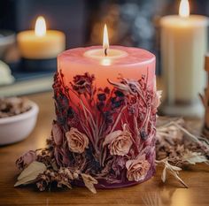 a lit candle sitting on top of a wooden table next to dried flowers and candles