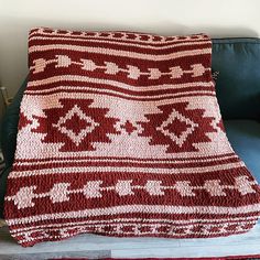 a red and white afghan sitting on top of a blue couch next to a wooden table