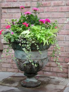 a large potted planter with pink flowers in front of a red brick wall