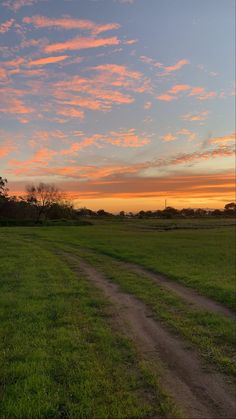 the sun is setting over an open field with a dirt road in front of it