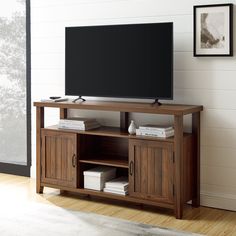 a flat screen tv sitting on top of a wooden entertainment center next to a potted plant