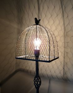 a birdcage with a lit candle in it sitting on a table next to a wall