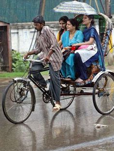 three people riding on the back of a rickshaw in the rain