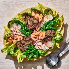 a plate with noodles, lettuce and radishes on it next to two spoons