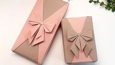 two pink boxes with bows on them sitting next to each other, one is folded and the other has an origami bow