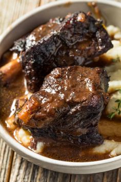 a bowl filled with meat and potatoes on top of a wooden table