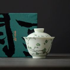 a white and green vase sitting on top of a wooden table next to a box