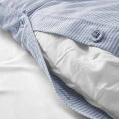 an unmade bed with white sheets and blue pinstripe comforter on it