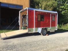 a red trailer is parked in front of a building with an open door on the side