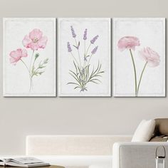 three pink flowers are hanging on the wall in a living room with white couches