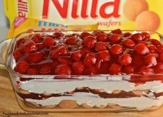 a large glass dish filled with cherries on top of a wooden table next to a bag of chips