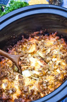 a slow cooker filled with ground beef and cheese is being stirred with a wooden spoon