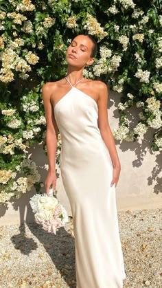 a woman standing in front of flowers wearing a white dress