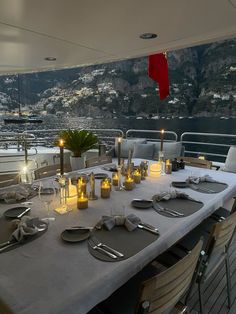 a dining table set up on the deck of a boat with candles and place settings