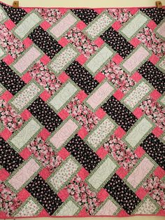 a pink and black quilt hanging on a wall