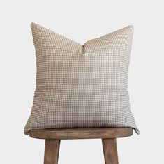 a brown and white checkered pillow sitting on top of a wooden stool next to a wall