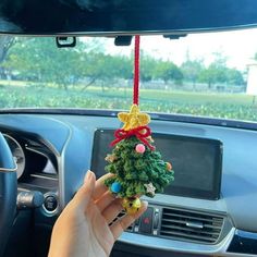 a hand holding a christmas tree ornament hanging from the dash board of a car