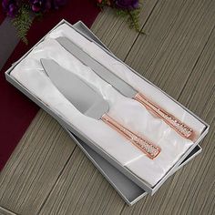 a knife and fork in a white box on a wooden table next to purple flowers