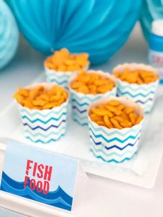 fish food sits on a tray next to blue balls and paper plates with cards in them