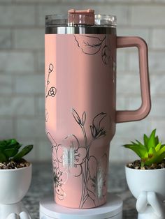 a pink coffee cup with flowers on it next to two planters and a brick wall