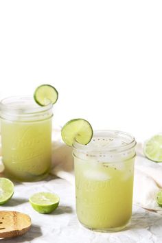 two mason jars filled with limeade sitting next to sliced limes and a wooden spoon