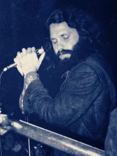 a man with long hair and beard holding a guitar in front of a microphone on stage