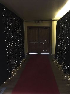 a red carpeted hallway with lights on the walls and door to another room in the background