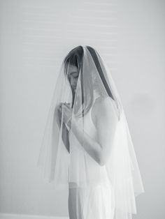 black and white photograph of a woman in wedding dress holding her veil over her face